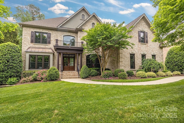 view of front of property with brick siding, french doors, a front lawn, and a balcony