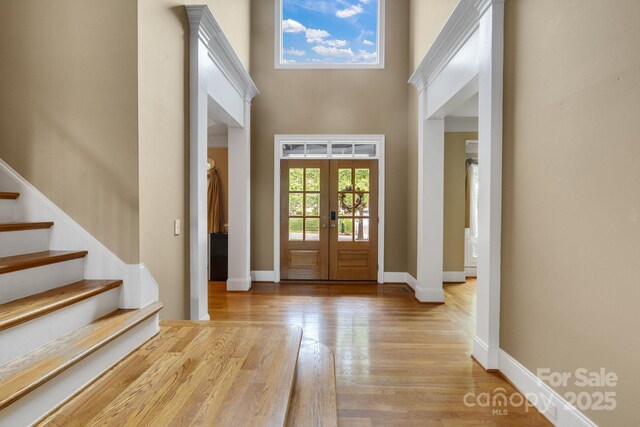 foyer entrance with stairway, baseboards, french doors, and light wood finished floors