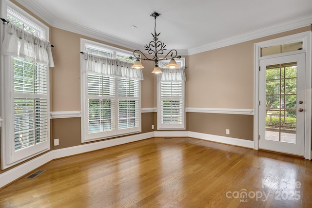 unfurnished dining area featuring visible vents, ornamental molding, an inviting chandelier, wood finished floors, and baseboards