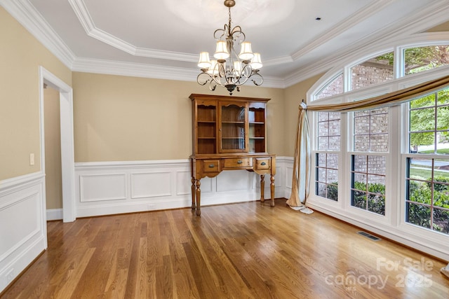 unfurnished dining area featuring a chandelier, a wainscoted wall, wood finished floors, visible vents, and ornamental molding