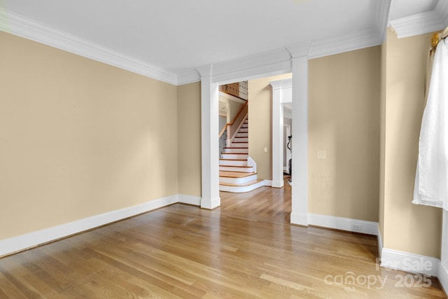 empty room featuring crown molding, baseboards, light wood finished floors, and stairs