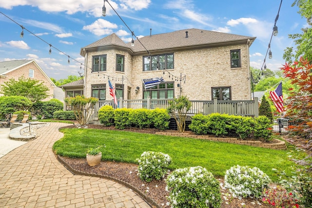 back of property featuring a lawn, a deck, and brick siding