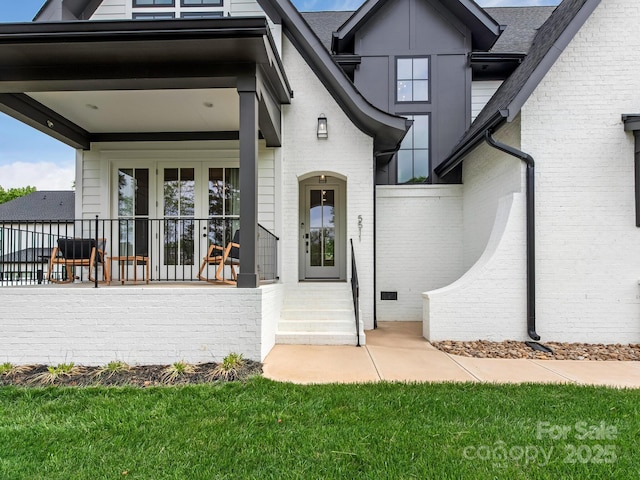 entrance to property with brick siding, a porch, and a shingled roof