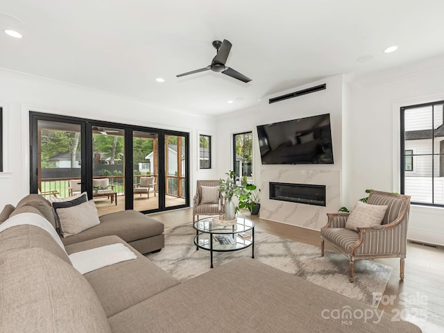 living area featuring a ceiling fan, ornamental molding, recessed lighting, wood finished floors, and a high end fireplace