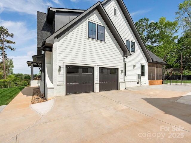 view of side of property with a sunroom, a garage, fence, brick siding, and driveway