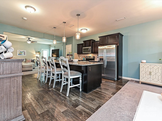 kitchen featuring ceiling fan, dark wood finished floors, appliances with stainless steel finishes, open floor plan, and a breakfast bar area