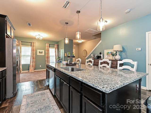 kitchen featuring dark cabinets, visible vents, appliances with stainless steel finishes, a kitchen island with sink, and a sink