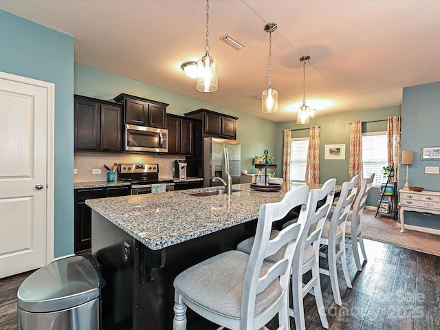 kitchen with visible vents, a sink, appliances with stainless steel finishes, a kitchen breakfast bar, and an island with sink