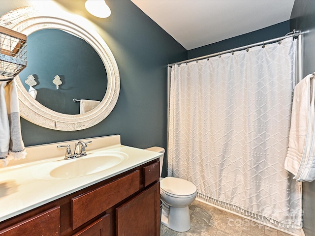 bathroom with toilet, vanity, a shower with shower curtain, and stone finish flooring