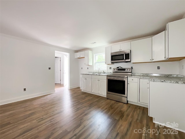 kitchen featuring dark wood finished floors, light stone countertops, white cabinetry, appliances with stainless steel finishes, and a sink