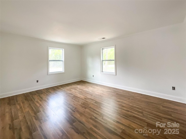 empty room with dark wood-style flooring, visible vents, a wealth of natural light, and baseboards