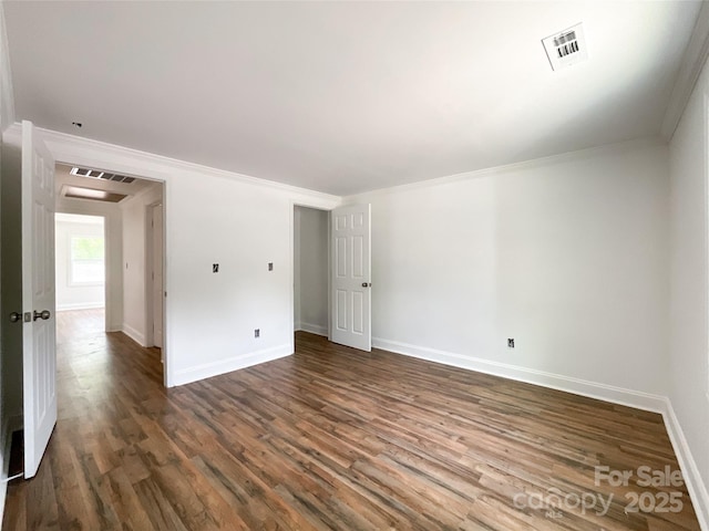 empty room with crown molding, dark wood-style flooring, baseboards, and visible vents