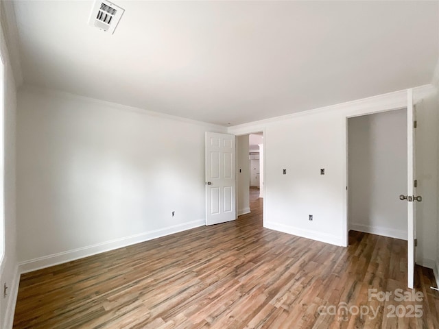 spare room featuring visible vents, baseboards, crown molding, and wood finished floors