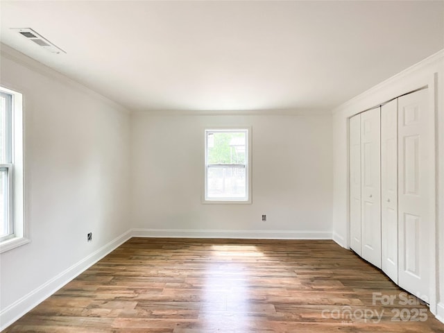 unfurnished bedroom with crown molding, wood finished floors, baseboards, and visible vents