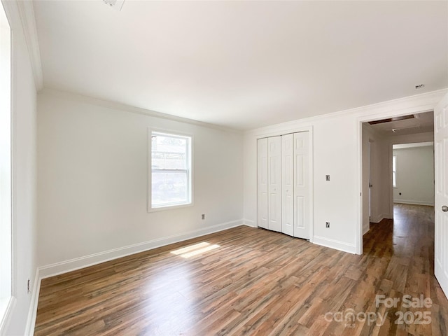 unfurnished bedroom with baseboards, a closet, ornamental molding, and wood finished floors