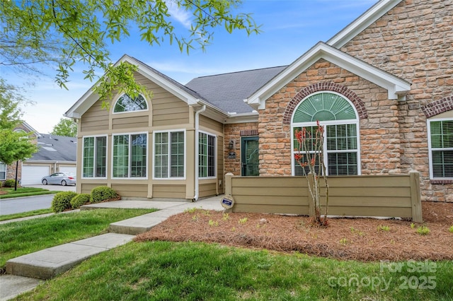 single story home featuring stone siding, fence, and a shingled roof