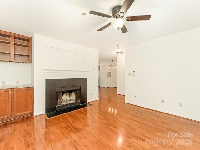 unfurnished living room featuring baseboards, light wood finished floors, a fireplace with flush hearth, and ceiling fan with notable chandelier