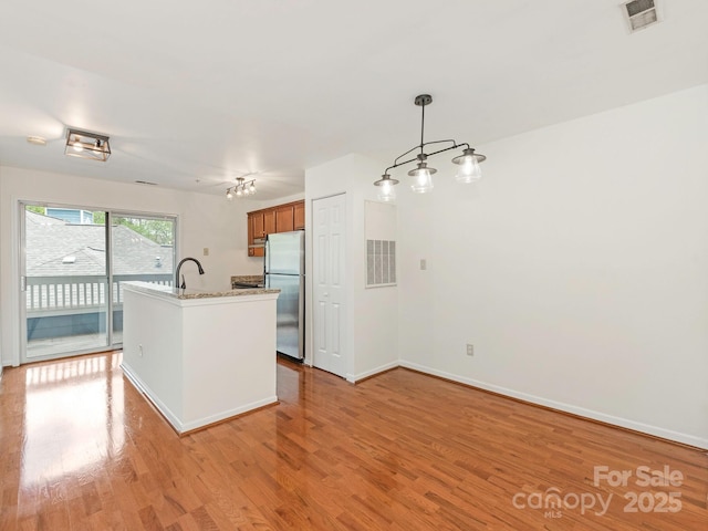 kitchen featuring baseboards, light wood-style flooring, freestanding refrigerator, visible vents, and brown cabinetry