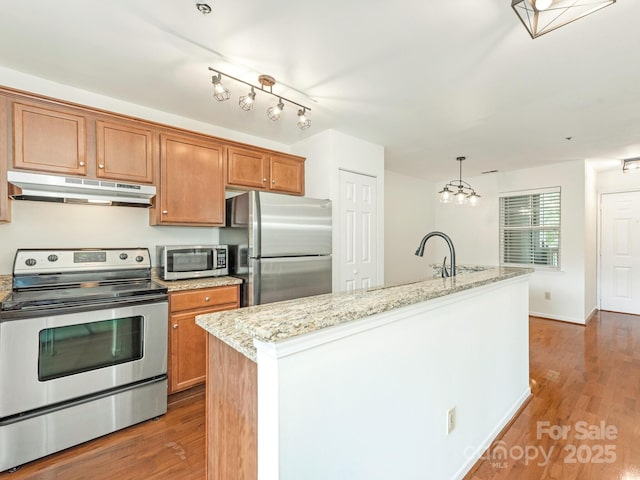 kitchen featuring stainless steel appliances, under cabinet range hood, brown cabinets, and wood finished floors