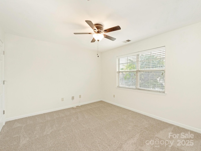 spare room with light colored carpet, baseboards, a ceiling fan, and visible vents