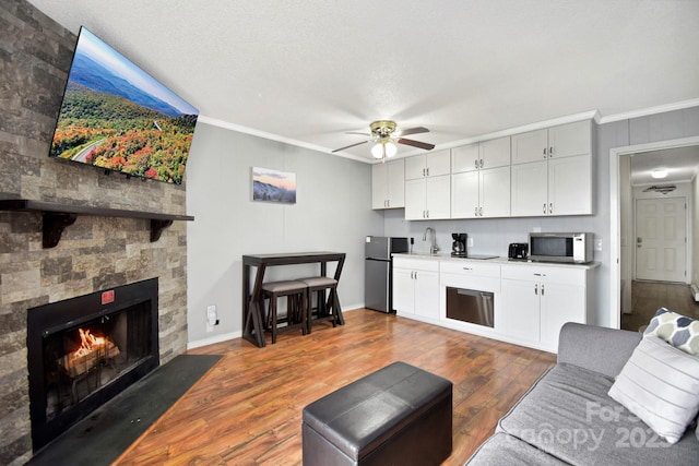 living area with ceiling fan, dark wood finished floors, ornamental molding, a stone fireplace, and baseboards