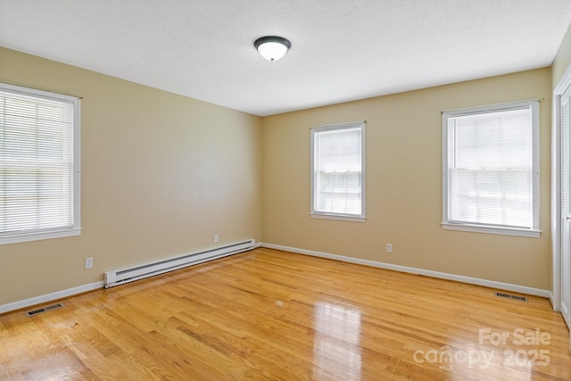spare room with a baseboard heating unit, visible vents, a wealth of natural light, and light wood-style floors