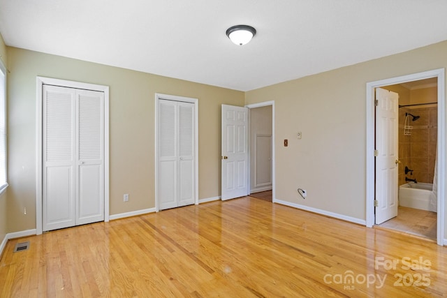 unfurnished bedroom with connected bathroom, visible vents, multiple closets, light wood finished floors, and baseboards