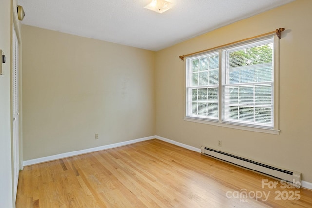 unfurnished room featuring light wood finished floors, a baseboard heating unit, and baseboards