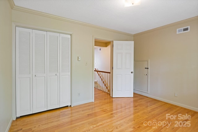 unfurnished bedroom featuring a closet, light wood-style flooring, baseboards, ornamental molding, and visible vents