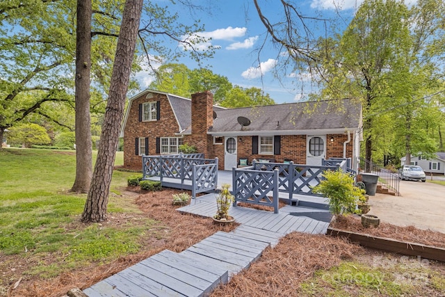 back of house with a chimney, brick siding, a shingled roof, a deck, and a yard