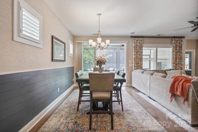 dining area with wood walls, baseboards, wood finished floors, and ceiling fan with notable chandelier