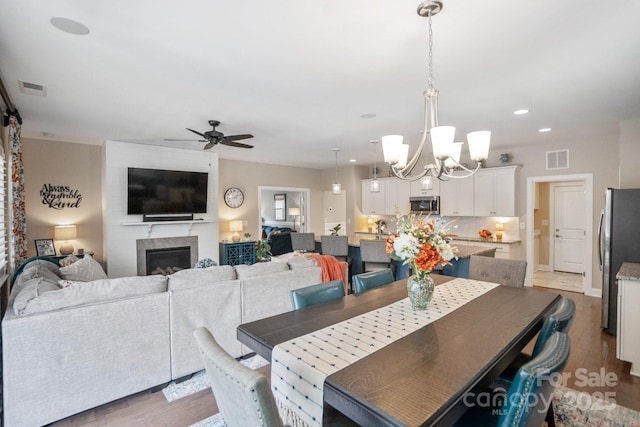 dining room featuring a fireplace, visible vents, ceiling fan with notable chandelier, and wood finished floors
