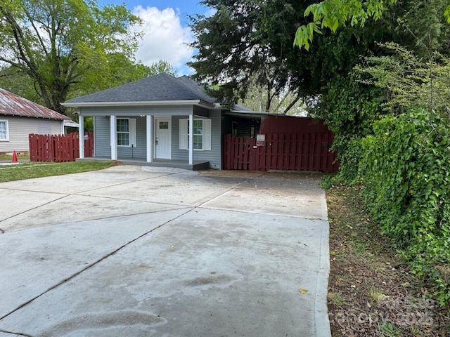 view of front of property featuring fence, covered porch, driveway, and roof with shingles
