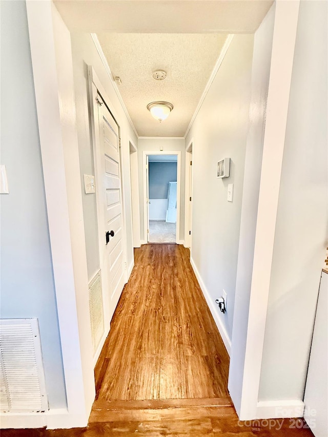 corridor featuring visible vents, a textured ceiling, crown molding, and wood finished floors