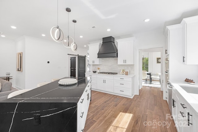13453 Portside Ln, Lancaster, SC 29720 - kitchen with a barn door, white cabinets, custom range hood, light wood-style flooring, and appliances with stainless steel finishes