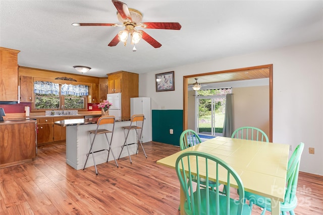 kitchen with freestanding refrigerator, a ceiling fan, brown cabinetry, and a sink
