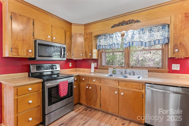 kitchen featuring brown cabinetry, appliances with stainless steel finishes, light wood-type flooring, a sink, and light countertops