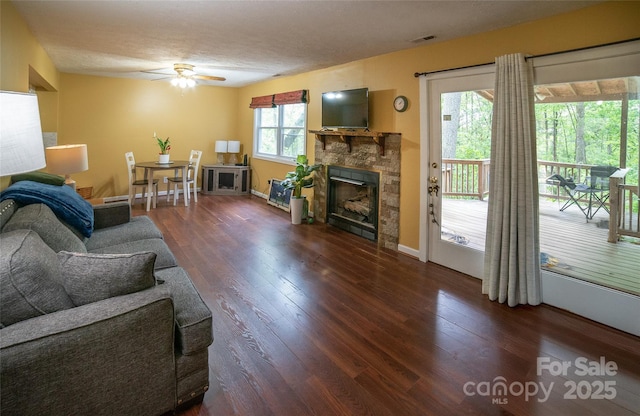living area featuring ceiling fan, a fireplace, visible vents, and wood finished floors