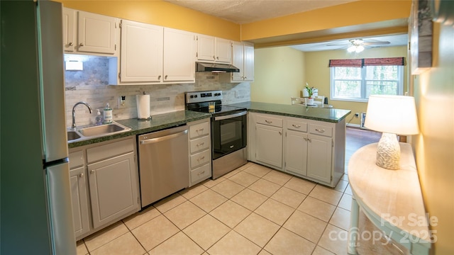 kitchen with a sink, a peninsula, white cabinetry, dark countertops, and appliances with stainless steel finishes