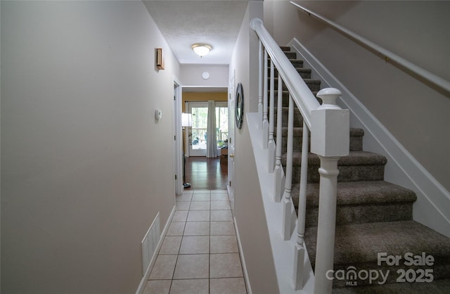 stairs with tile patterned flooring, a textured ceiling, baseboards, and visible vents