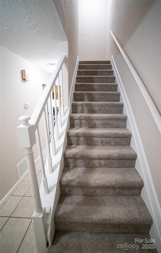 staircase with a textured ceiling, visible vents, and tile patterned flooring