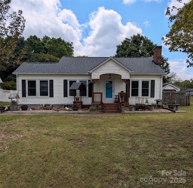 view of front of house featuring a chimney, a shingled roof, fence, and a front lawn