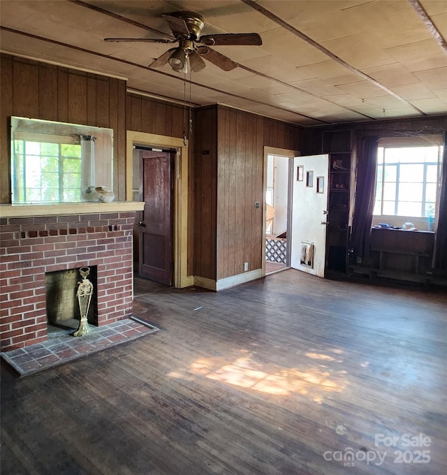 unfurnished living room with a wealth of natural light, a ceiling fan, dark wood-style floors, and wood walls