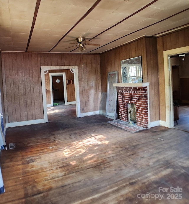 unfurnished living room with a ceiling fan, wood finished floors, wooden walls, a fireplace, and visible vents