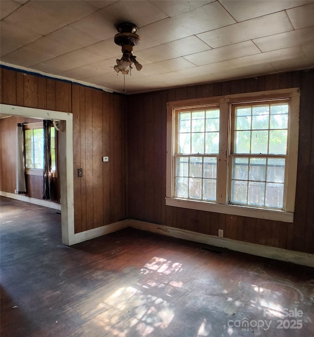 empty room featuring wood walls, a wealth of natural light, and ceiling fan