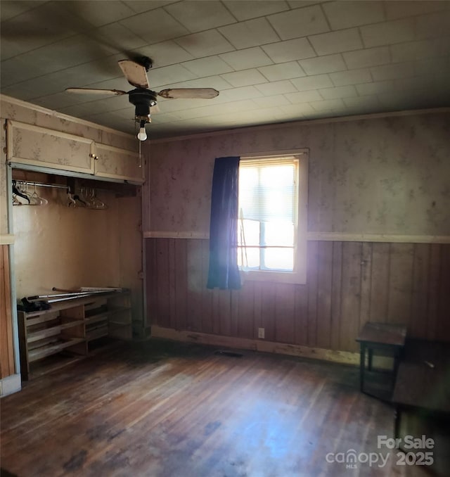 unfurnished bedroom with dark wood finished floors, a ceiling fan, and wooden walls