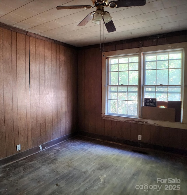 unfurnished room featuring baseboards, visible vents, a ceiling fan, wood walls, and wood finished floors