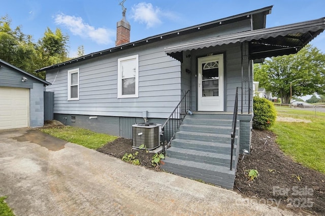 rear view of house featuring a chimney, an outbuilding, central air condition unit, a garage, and crawl space