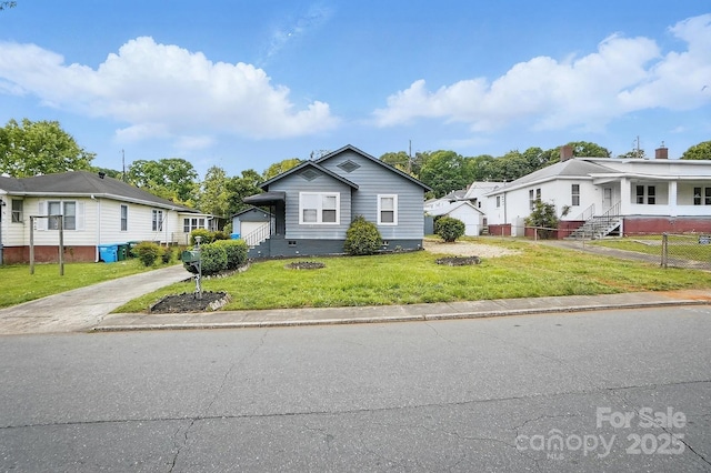 bungalow featuring fence, concrete driveway, a front yard, and a residential view