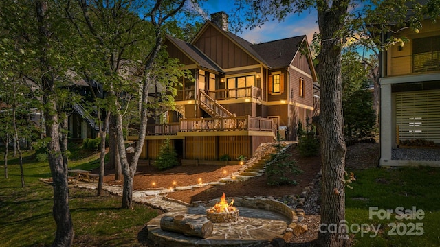 rear view of house with stairs, board and batten siding, a deck, a chimney, and a fire pit
